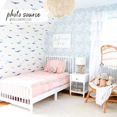 a bedroom with blue and white wallpaper, pink bedding and a wicker chair