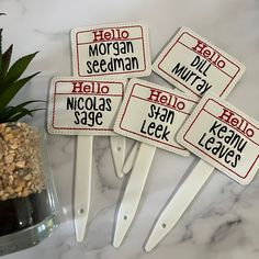 four ironing pins with name tags on them sitting next to a potted plant