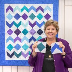 a woman holding up a piece of paper in front of a quilt