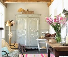 a living room filled with furniture and flowers on top of a wooden table in front of a white armoire