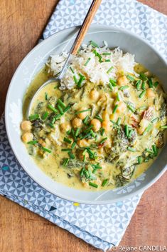 a white bowl filled with green curry and chickpeas next to rice on a blue napkin