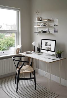 a desk with a computer on top of it in front of a window and a rug