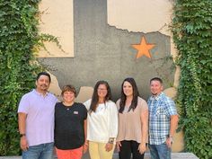 a group of people standing next to each other in front of a wall with ivy growing on it