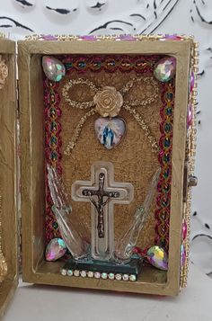 an open box with a cross in the middle and other decorations around it on a table