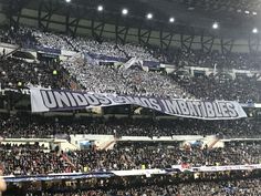 a large group of people in a stadium holding up a banner that reads under the umbrellas