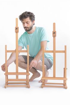 a man kneeling down in front of an easel that is made out of wood