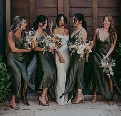 a group of women standing next to each other in front of a wooden door holding bouquets