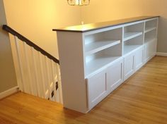 a white entertainment center in the corner of a room with wood flooring and handrails