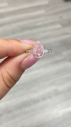 a woman's hand holding an engagement ring with a pink diamond in the middle