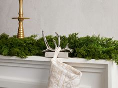 a christmas stocking hanging from a mantel decorated with greenery and gold candlesticks