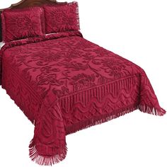 a bed with red bedspread and pillows on top of it, next to a wooden headboard