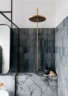 a black and white tiled bathroom with gold shower faucet, marble counter top