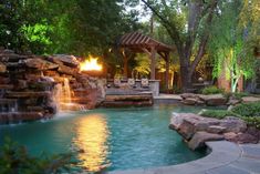 an outdoor pool with waterfall and gazebo surrounded by greenery at sunset or dusk