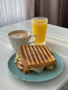 a sandwich on a plate next to a cup of coffee and a glass of orange juice