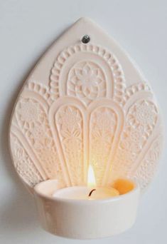 a small white candle holder with a lit candle in it's center on a wall