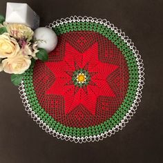 a red and green doily with white flowers on the table next to candlesticks