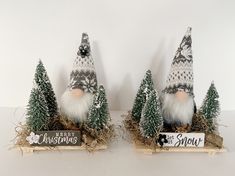 two christmas gnomes sitting on top of hay in front of trees and a sign that says happy christmas