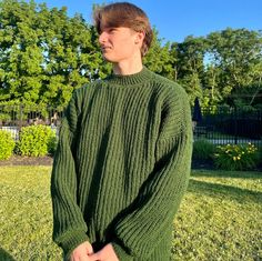 a man standing in the grass wearing a green sweater