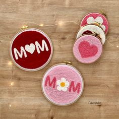 three embroidered ornaments with the word mom written in red and white on them, sitting on a wooden surface