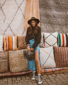 a woman sitting on top of a couch next to pillows and rugs in front of a wall