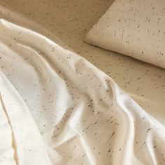 an unmade bed with white sheets and black speckles on the sheeting