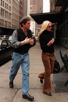 the man and woman are walking down the sidewalk talking to each other while holding hands