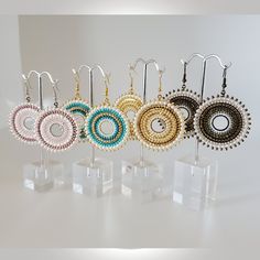 five pairs of earrings are on display with clear acrylic stands and white background