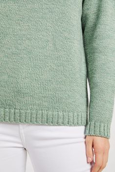 a woman in white jeans and a green sweater is looking down at her left shoulder