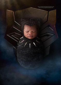 a newborn baby is wrapped in a black blanket with spikes on it's head