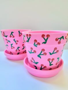 two pink cups and saucers with cherries on them sitting next to each other