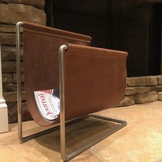 a brown chair sitting in front of a fire place next to a stone fireplace with a magazine rack