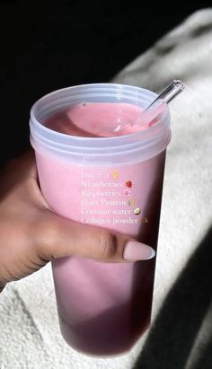 a hand holding a pink cup with a spoon in it