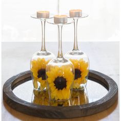 three wine glasses with sunflowers in them sitting on a tray next to candles