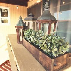 a wooden box filled with green plants on top of a table next to two lanterns