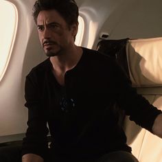 a man sitting on an airplane seat with his hands in his pockets and looking at the camera