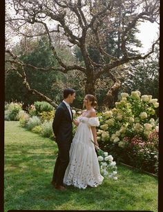 a bride and groom standing next to each other in front of a tree with white flowers