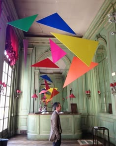 a man is walking through a room with many colorful kites hanging from the ceiling