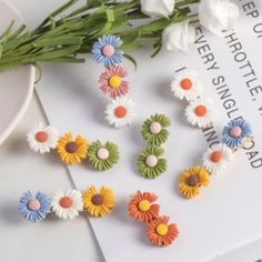 several different colored flowers on top of a white table next to a book and flower bouquet