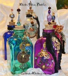 three colorful glass bottles are sitting on a white sheet and one is filled with charms