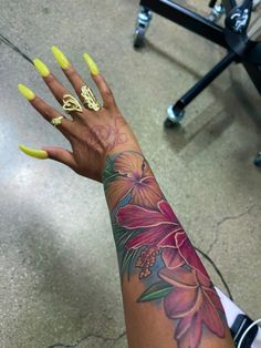 a woman's arm with yellow nail polish and flower tattoo on the left hand