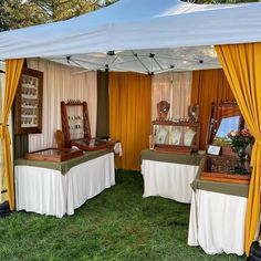 two tables covered in white cloths under a tent with mirrors and other items on it