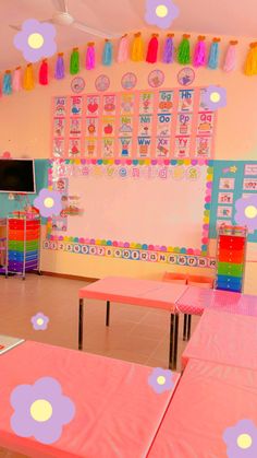 an empty classroom with pink tables and colorful decorations on the wall above them is decorated with pom poms