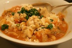 a white bowl filled with chicken and rice covered in gravy, garnished with green onions