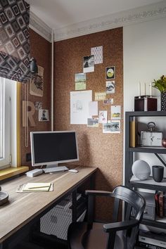 a desk with a computer on top of it next to a book shelf and window