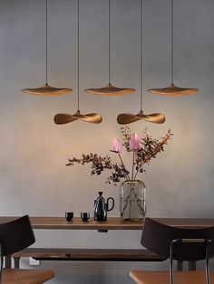 a dining room table with four lights hanging from it's ceiling and flowers in a vase on the table