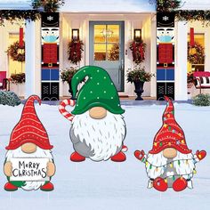 three christmas gnomes standing in front of a white house with holiday decorations on it