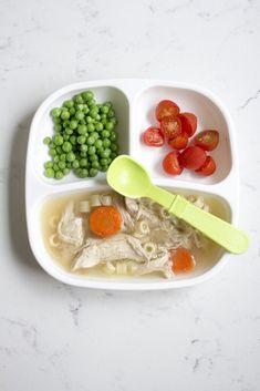 a white plate topped with pasta, peas and carrots next to a green spoon