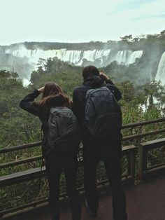 two people are looking at the falls from a viewing platform in front of trees and bushes