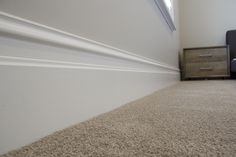 the corner of a room with a bed, nightstand and carpeted floor in front of it