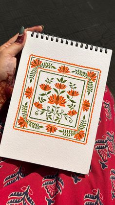 a woman is holding a notebook with an orange and green floral design on the cover